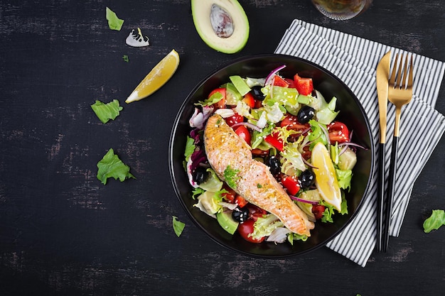 Baked salmon fish fillet and fresh green lettuce tomato avocado and black olives Greek salad Top view