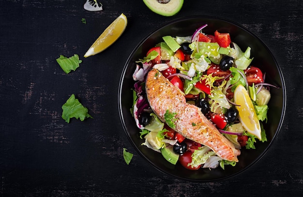 Baked salmon fish fillet and fresh green lettuce tomato avocado and black olives Greek salad Top view