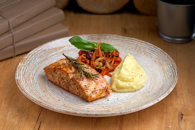 Baked salmon grilled with mashed potatoes and salad on a wooden background