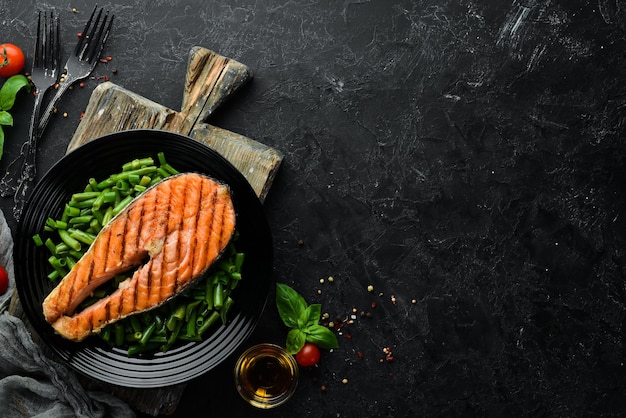 Baked salmon steak with green beans on a black plate Top view Free copy space