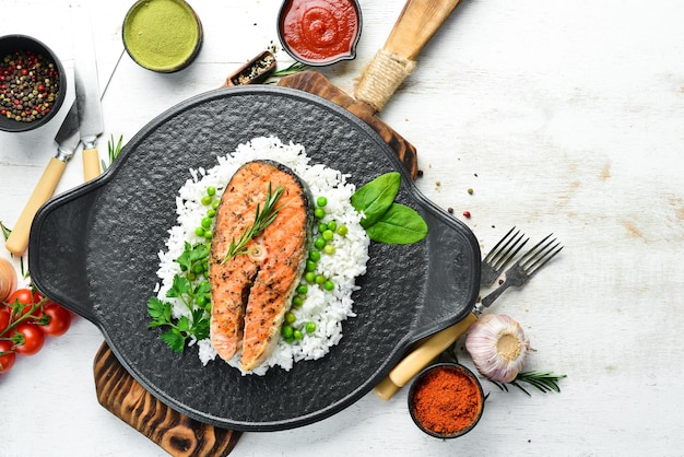 Baked salmon steak with rice and vegetables on a black stone plate Seafood Top view Free space for your text