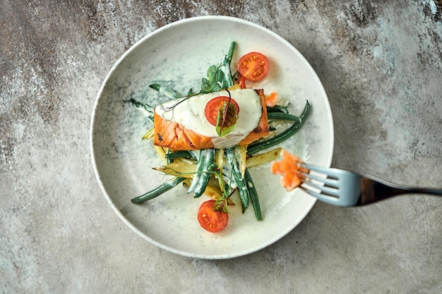 Baked salmon steak with vegetables in a creamy sauce on a plate. Close-up, selective focus.