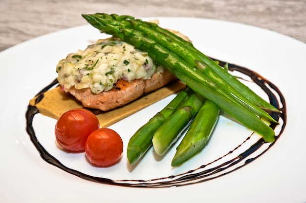 Baked Salmon with Cheese Gratin Garnished with Asparagus and Cherry Tomatoes on a White Plate food