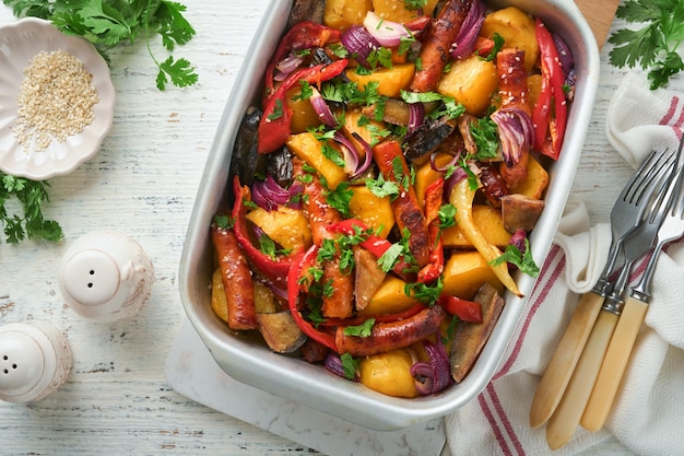 Baked sausage and vegetables peppers zucchini tomatoes red onion and eggplant with sesame and cilantro served hot from oven on baking tray Traditional lunch dish BBQ Sausage jersey tray bake