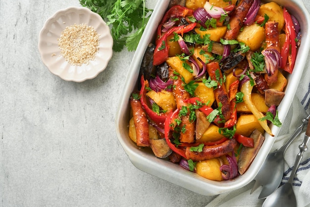 Baked sausage and vegetables peppers zucchini tomatoes red onion and eggplant with sesame and cilantro served hot from oven on baking tray Traditional lunch dish BBQ Sausage jersey tray bake