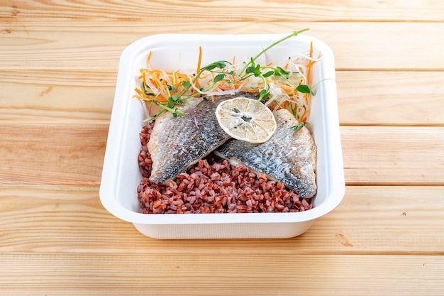 Baked sea bass with red rice Healthy diet Takeaway food Eco packaging On a wooden background
