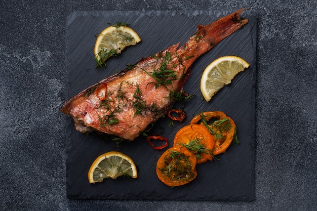 Baked sea bass with tomato pepper lemon and herbs on black slate stand on dark