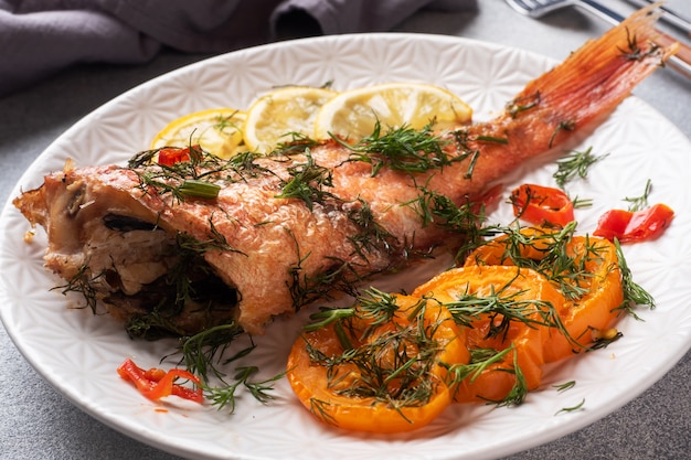 Branzino al forno con pomodoro pepe limone ed erbe in un piatto di ceramica su un grigio