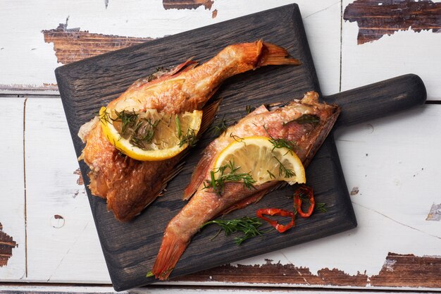 Baked sea bass with tomato pepper lemon and herbs on wooden Board