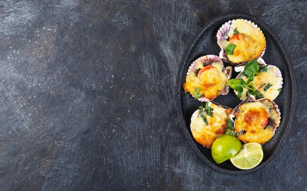 Baked seafood shellfish scallops with cheese and lemon black background