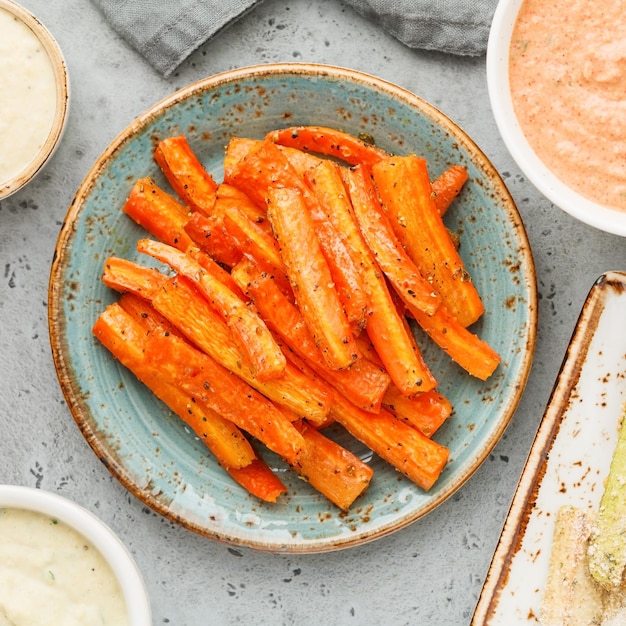 Baked season carrot sticks with sauce and hummus Vegetarian healthy food Flat lay top view