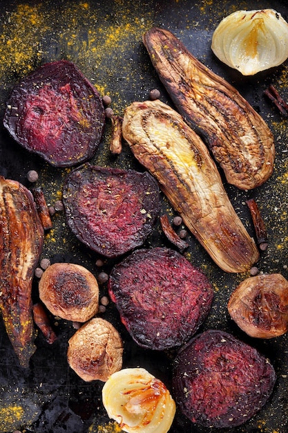 Baked slices of beetroot eggplant onion with spices peppercorns on a dark background Healthy food lifestyle Salt oil spices Closeup