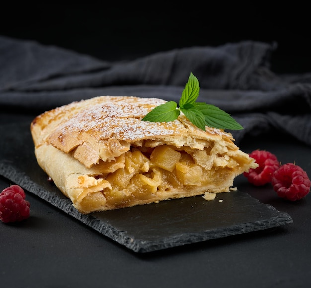 Baked strudel with apples sprinkled with powdered sugar on a black board delicious dessert