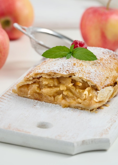 Baked strudel with apples sprinkled with powdered sugar on a white wooden board