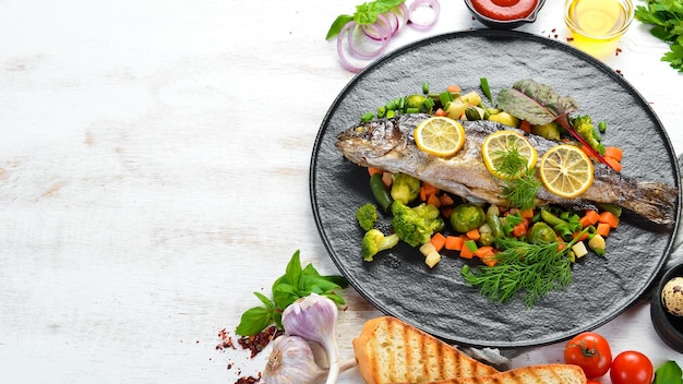 Baked trout fish with vegetables and lemon on a black plate Top view Free copy space