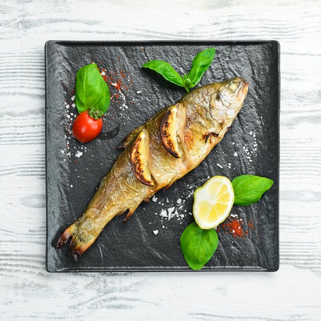 Baked trout with lemon and vegetables on a black stone plate\
seafood river fish top view