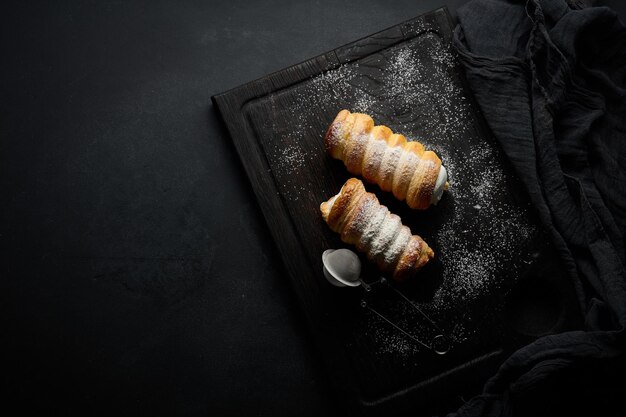 Baked tubules filled with whipped egg white cream on a black wooden kitchen board top view