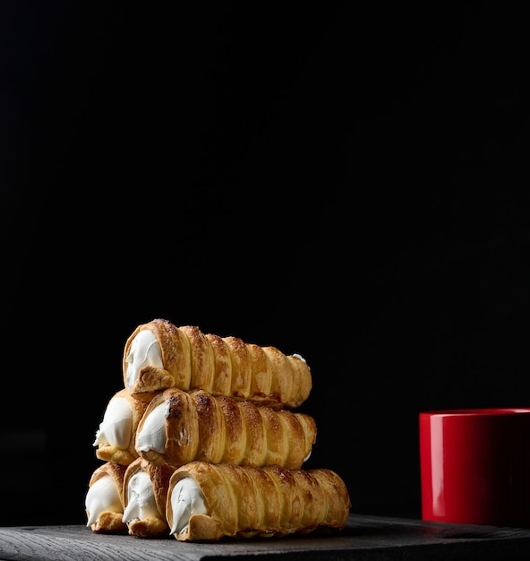 Baked tubules filled with whipped egg whites cream on a black wooden kitchen board