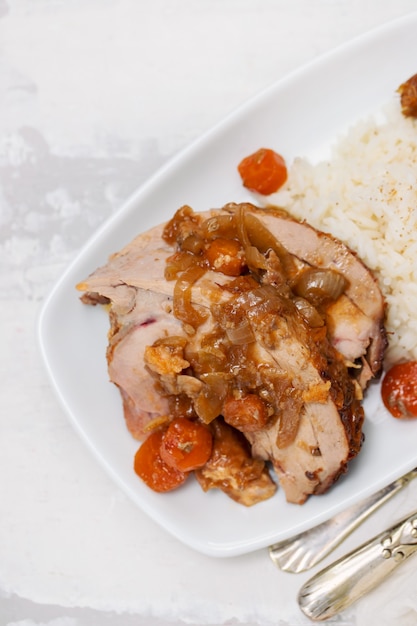 Baked turkey leg with vegetables, smoked sausage, herbs and boiled rice on white dish