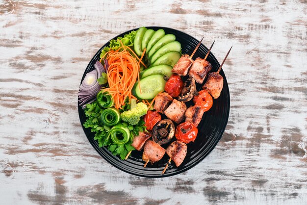 Baked veal shish kebab on a plate with fresh vegetables On a wooden background Top view Copy space