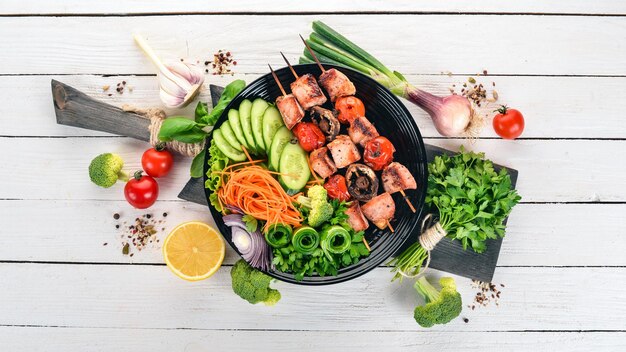 Baked veal shish kebab on a plate with fresh vegetables On a wooden background Top view Copy space