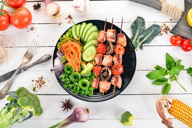 Baked veal shish kebab on a plate with fresh vegetables On a wooden background Top view Copy space