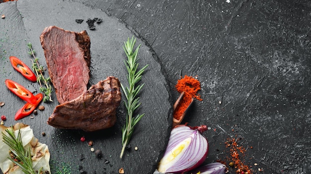 Baked veal steak with spices on a black stone plate Pepper steak Top view free space for your text Rustic style