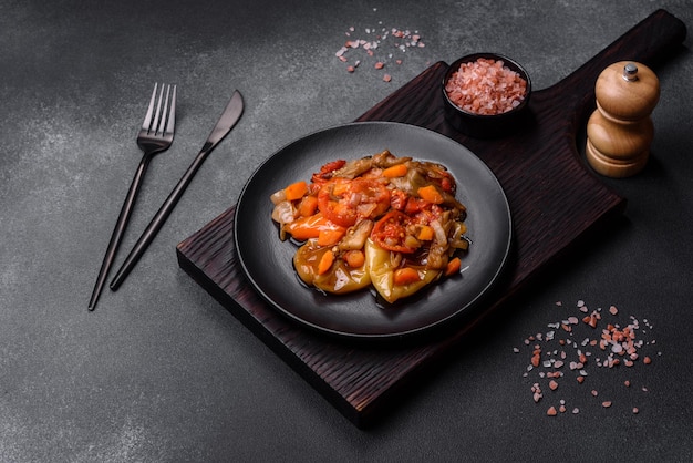 Baked vegetables eggplant peppers and carrots on a black plate on concrete background