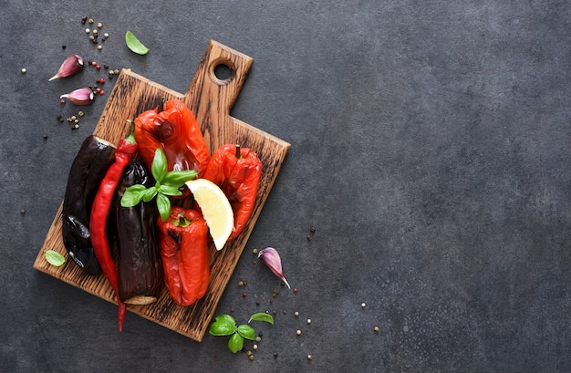 Verdure al forno: melanzane e peperoni su una tavola di legno su fondo nero.