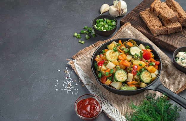 Baked vegetables in a serving pan, greens and rye bread on a brown background. Horizontal view, space for copying. Healthy food.