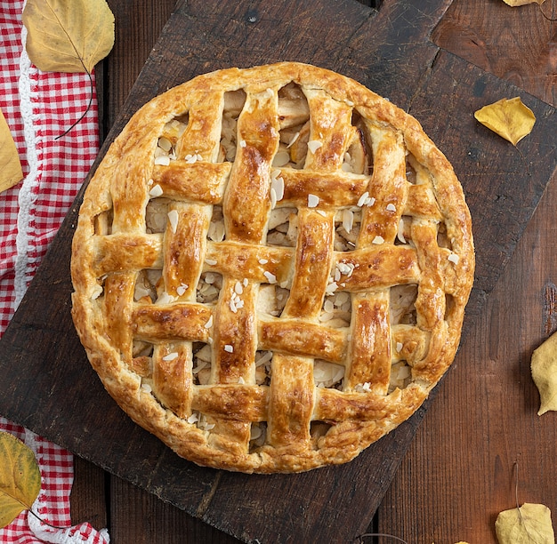 Baked whole round apple pie on a brown wooden board