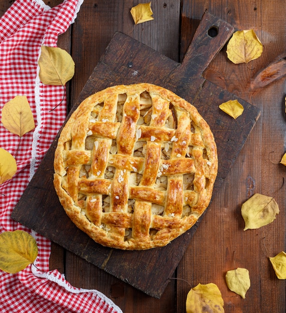 Baked whole round apple pie on a brown wooden board