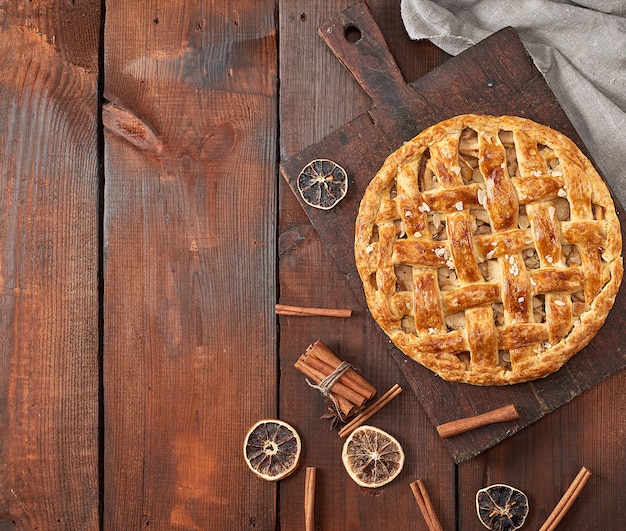 Baked whole round apple pie on a brown wooden board