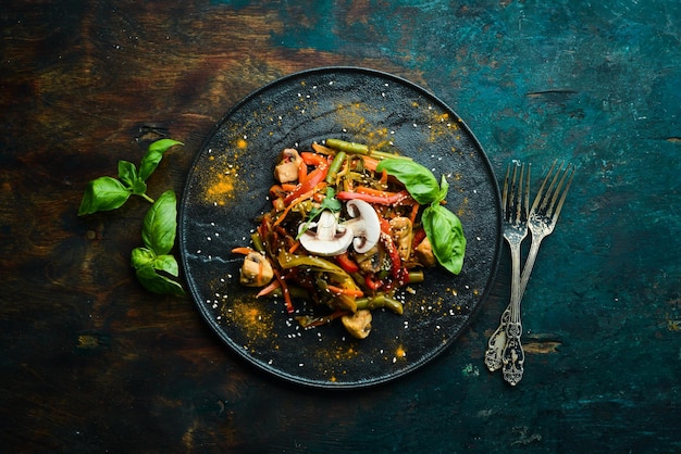 Baked wok vegetables on a black stone plate Asian cuisine Top view