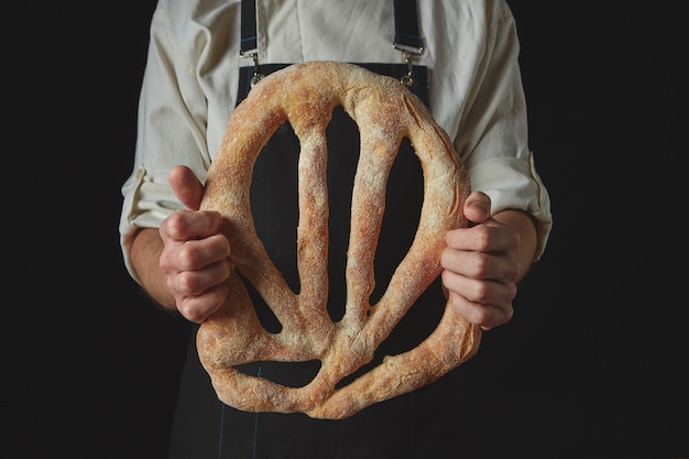 Baker in an apron holding fougas bread in hand on a black background isolated