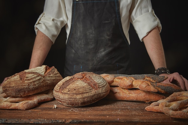 Пекарь в фартуке со свежим хлебом на деревянном коричневом столе
