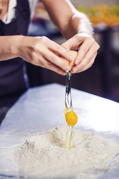 Baker breekt een ei in een hoop bloem.