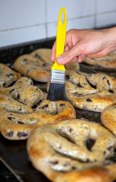 Baker brushing freshly baked olive breads with olive oil