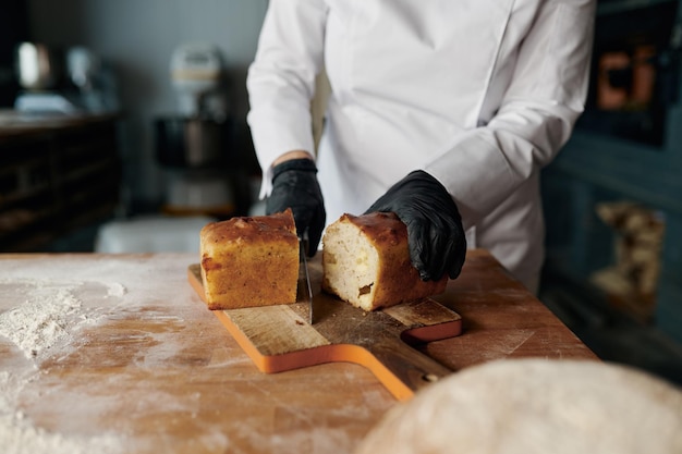 Baker chef-kok houdt mes vast en snijdt vers brood op houten tafel