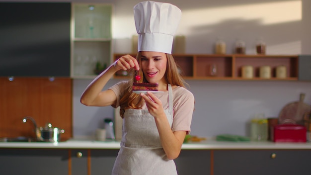 Baker decorating cake with cherry on kitchen Chef woman in finishing dessert