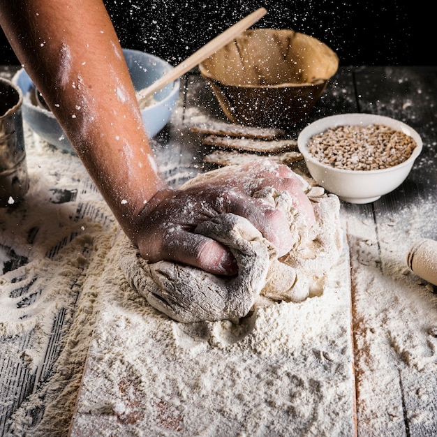 Baker die het tarwebloem op het deeg over de keukenlijst uitsprenge