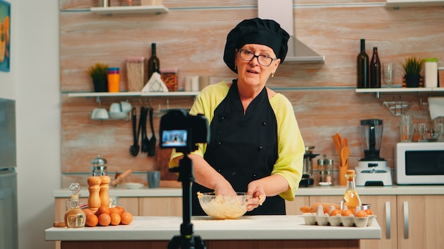 Baker draagt een bonete-opnamepodcast van traditioneel voedselrecept met meel en gebarsten eieren. Influencer-chef die internettechnologie gebruikt om te communiceren, te fotograferen op sociale media met digitale apparatuur