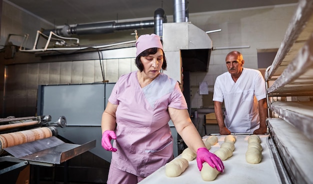 The baker forms the dough for baking bread and put it into oventray at the manufacturing