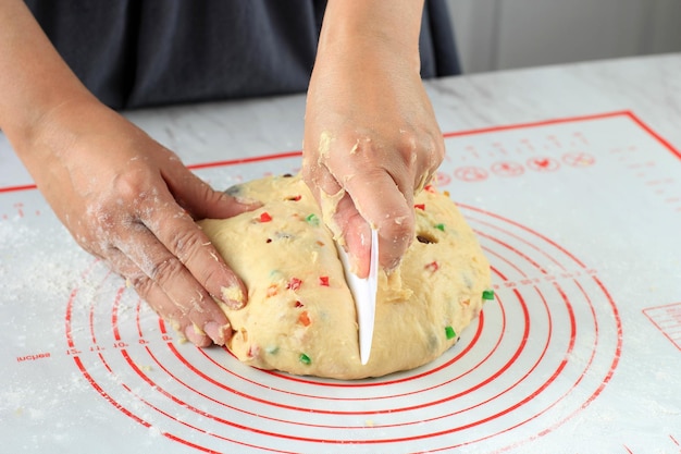 Baker hand snijdt rauwe gist fruit brood deeg op witte tafel achtergrond met een plastic mes
