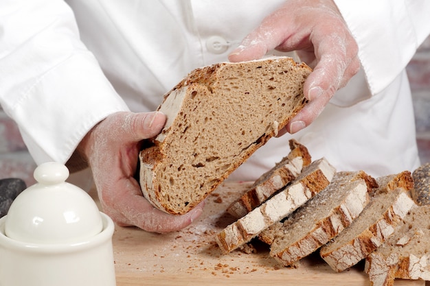 Mani del panettiere con pane fresco sulla tavola di legno