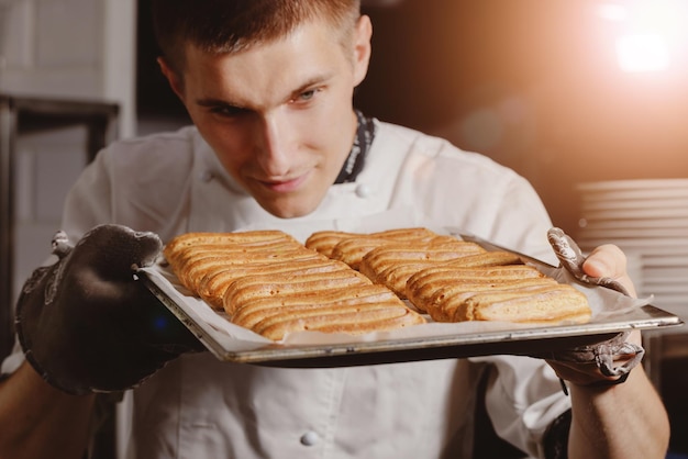 Пекарь держит свежеиспеченные эклеры на концепции противня для пекарни