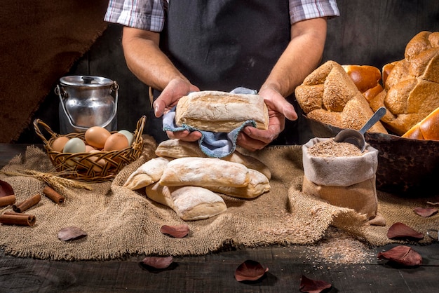 Baker holds breads on rustic table.