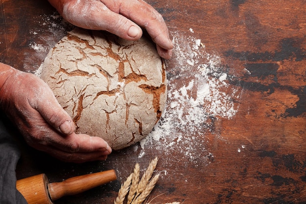 Baker houdt vers gebakken zelfgebakken brood in handen op houten tafel. Bovenaanzicht plat gelegd met kopieerruimte