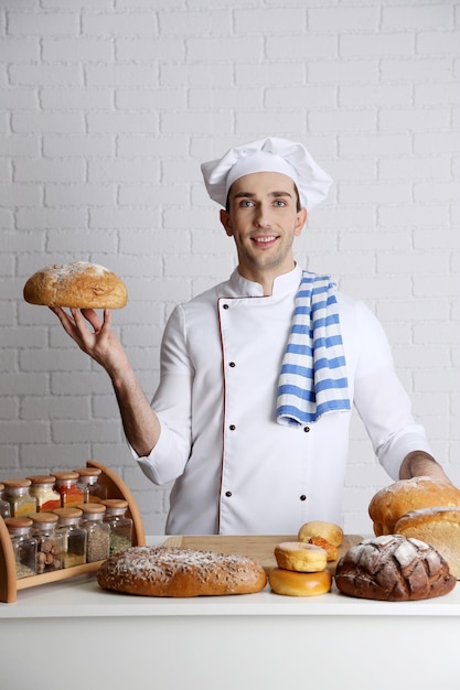 Фото Пекарь на кухне за столом со свежими буханками хлеба на фоне стены из белого кирпича