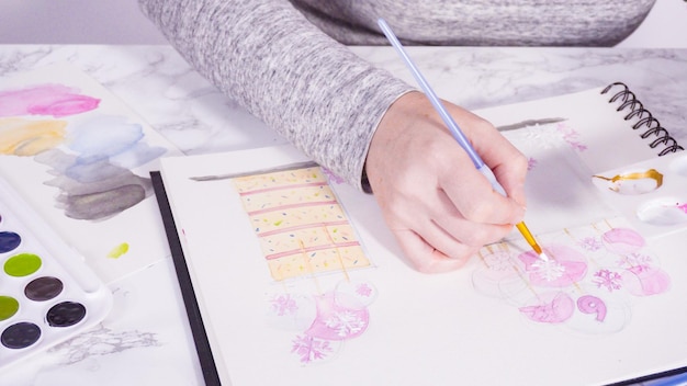 Baker is drawing the design of a birthday cake with watercolors.